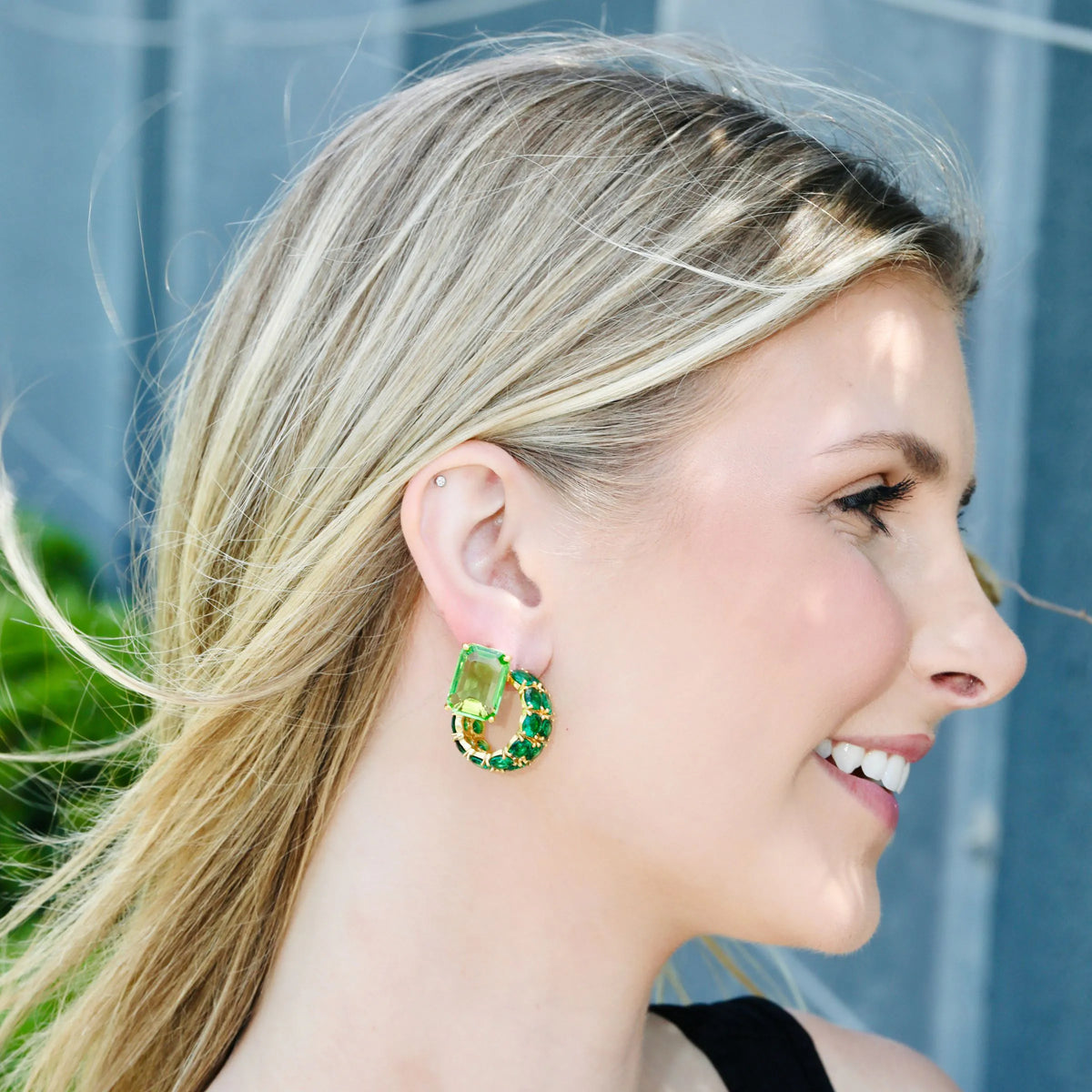 Close-up of emerald green and gold earrings showing the faceted stones